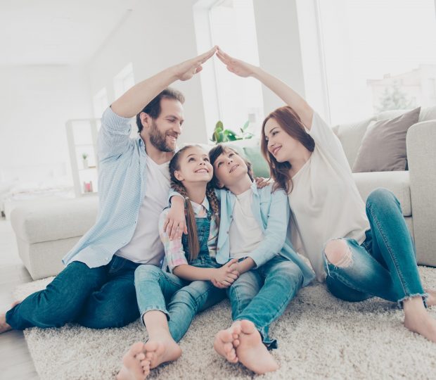 Des parents protégeant symboliquement leurs enfant en formant le toit d'une maison avec leur maison au milieu de leur salon